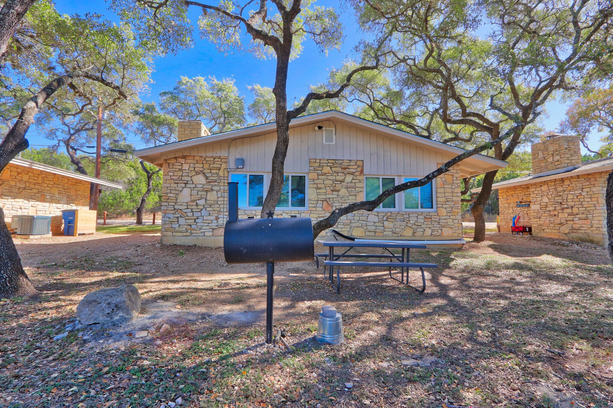 A stone building with a stone chimney, a mailbox, and a picnic table in a wooded area.