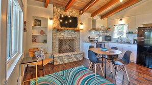 A cozy living room with a stone fireplace, wooden beams, and a dining area with modern chairs. - Quaint Cottages in Canyon Lake! Perfect for kids! (Canyon Lake)
