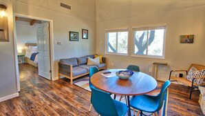 Una habitación amplia con suelo de madera, una mesa redonda para comer con sillas azules, un sofá con cojines y una ventana que proporciona luz natural.