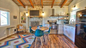 Una cocina moderna con pared de piedra, vigas de madera, zona de comedor con sillas y un refrigerador.