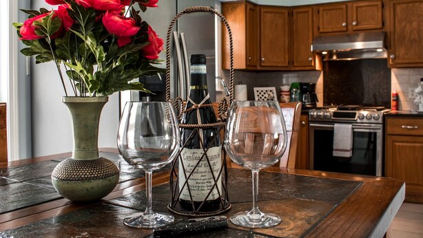 Un comptoir de cuisine orné d’un vase de fleurs rouges, d’une bouteille de vin et de deux verres à vin.