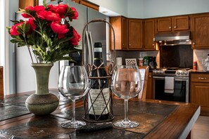 Un comptoir de cuisine orné d’un vase de fleurs rouges, d’une bouteille de vin et de deux verres à vin.