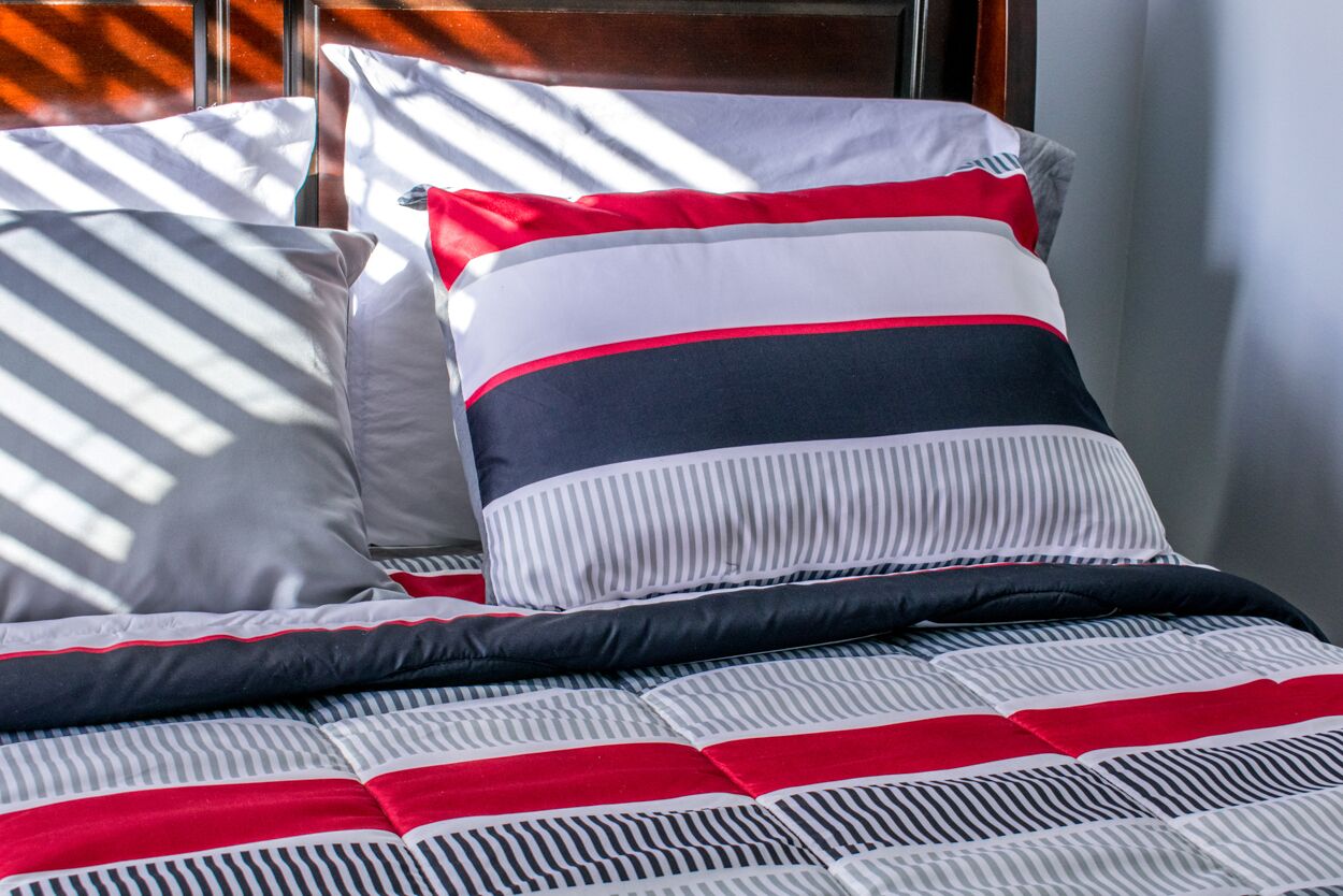 A neatly made bed with striped bedding and pillows in a hotel room.