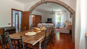 A dining area with a rustic wooden table, chairs, and a kitchen visible in the background.