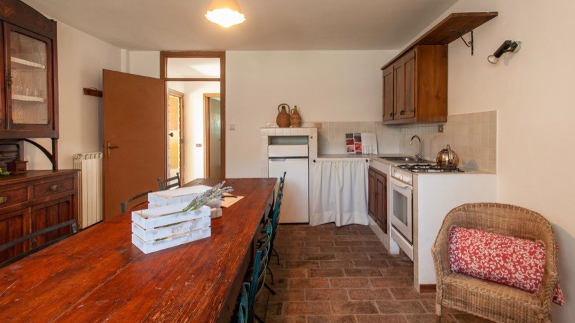 A compact kitchen with a wooden table, a refrigerator, a stove, and a wicker chair.
