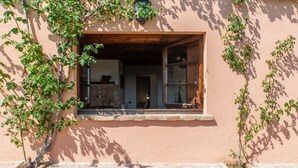 Una ventana con marco de madera, una pared de piedra y vista a una habitación con chimenea de piedra.