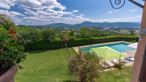 Una piscina con vistas a montañas, un césped cuidado y un seto.