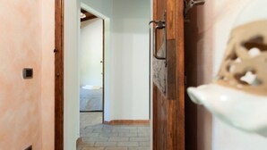 Un pasillo con una puerta de madera, suelo de baldosas y una vista parcial de una habitación con cama.