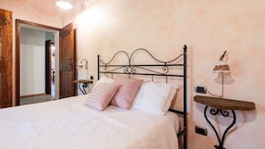 A neatly made bed with a metal headboard, a bedside table with a lamp, and a wall-mounted alarm clock.