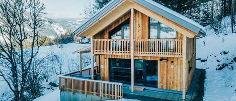 A wooden cabin with a balcony, surrounded by snow and trees.