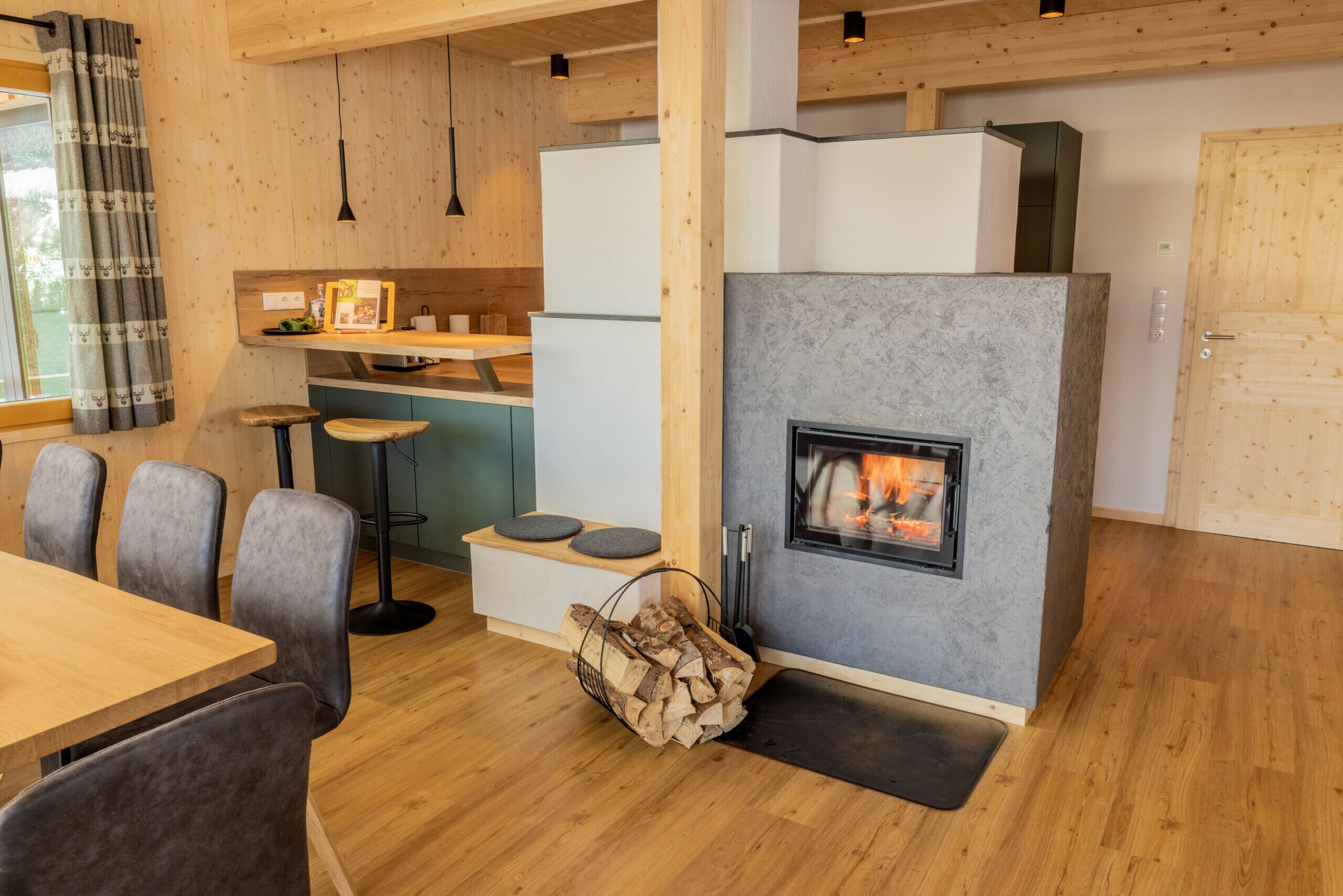 A modern kitchen with a built-in fireplace, wooden flooring, and a dining area with grey upholstered chairs.