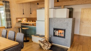 A modern kitchen with a built-in fireplace, wooden flooring, and a dining area with grey upholstered chairs. - Woody 21 - the Tiger Woody (St. Georgen am Kreischberg)