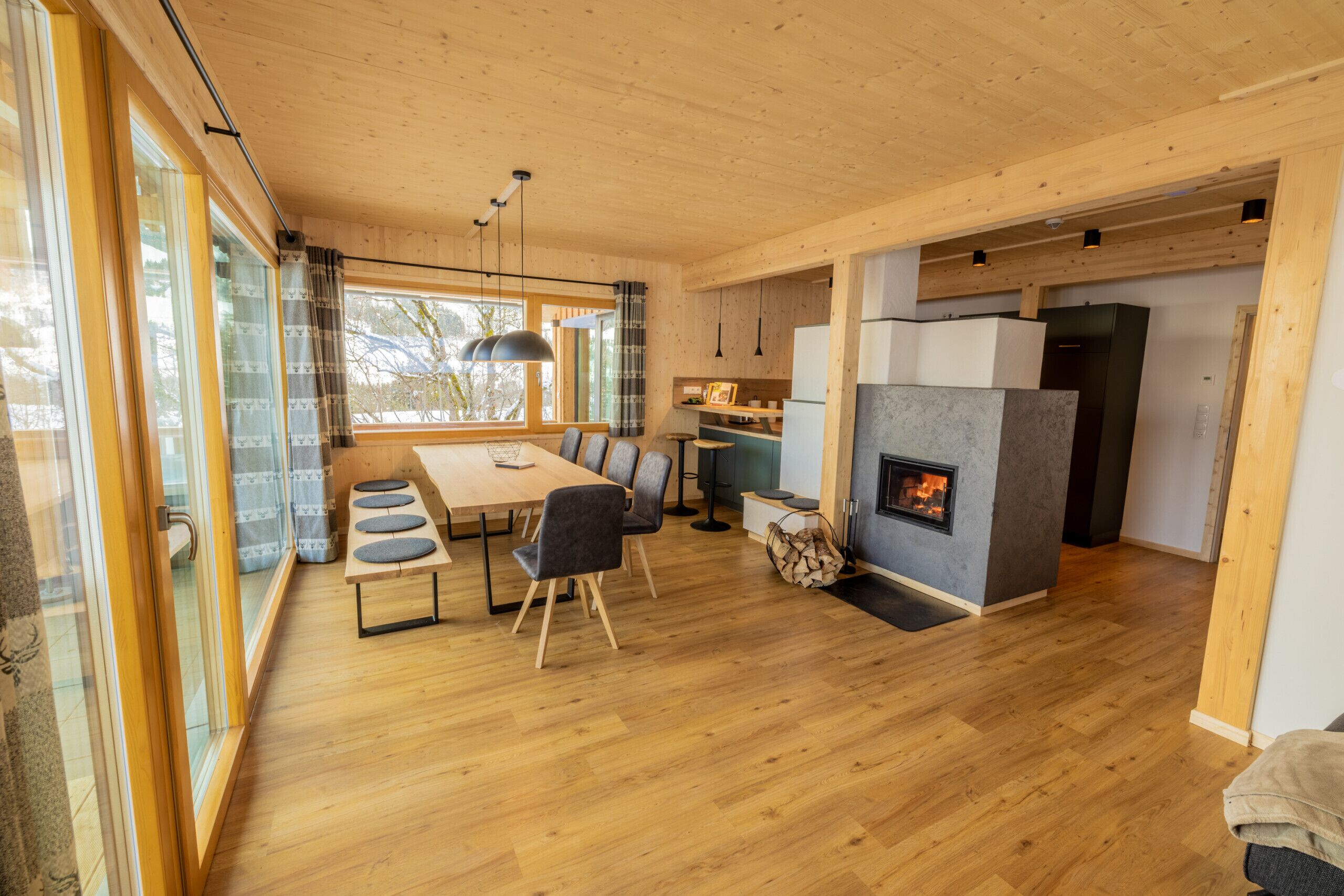 Un vaste espace de vie doté d’un plancher en bois, d’une table à manger avec des chaises, d’une cheminée et de grandes fenêtres.