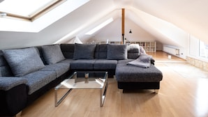 Un dormitorio tipo loft moderno con un tragaluz grande, un sofá modular, una mesa de centro de vidrio y piso de madera.