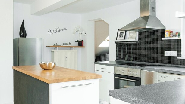 Una cocina moderna con armarios blancos, encimera de madera y campana extractora de acero inoxidable.