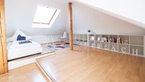 Un dormitorio estilo loft moderno con techo inclinado, tragaluces, cama blanca, estantería de madera y alfombra roja.