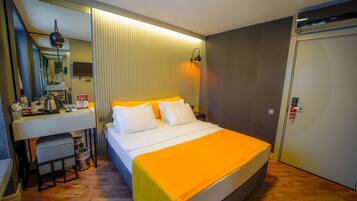 Quarto de hotel com cama, escrivaninha com espelho, pequeno espaço para kitchenette e guarda-roupa.