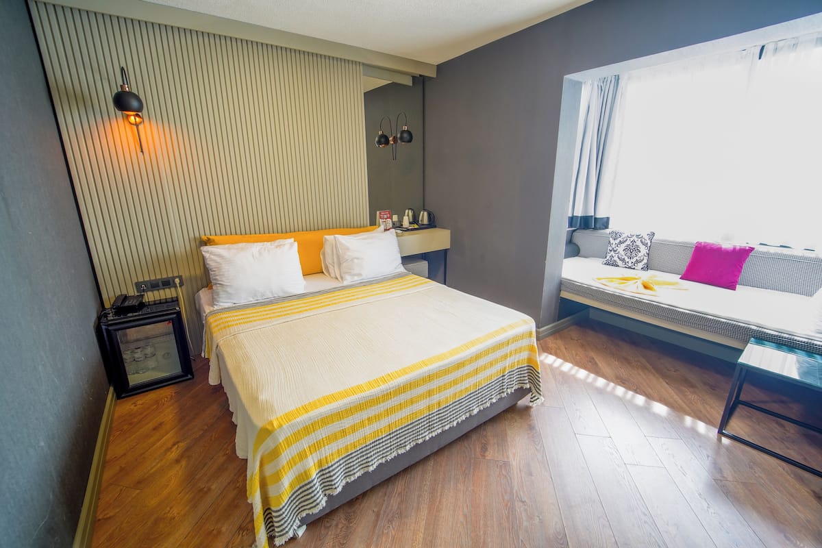 Una habitación de hotel moderna con una cama grande, una mesita de noche, un escritorio pequeño y una ventana con cortinas.