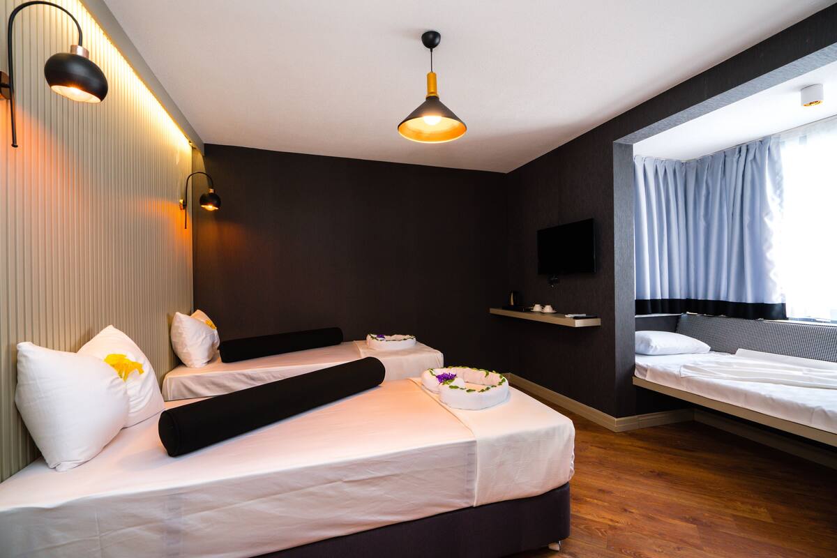 Una habitación de hotel moderna con dos camas, una televisión de pantalla plana, una mesita de noche y un ventanal grande con cortinas.