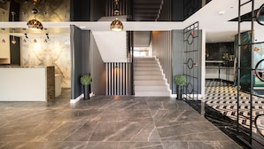 A modern interior with a marble reception desk, a staircase with a geometric railing, and a patterned floor.
