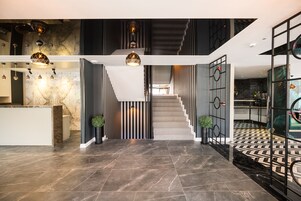 Un interior moderno con un mostrador de recepción de mármol, una escalera con barandilla geométrica y un suelo estampado.