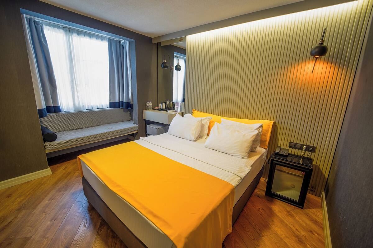 Un dormitorio con cama, una ventana con cortinas, una mesita de noche y una lámpara de pared.