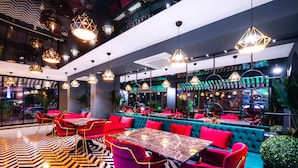 A modern restaurant with red and teal seating, geometric pendant lighting, and a patterned floor.