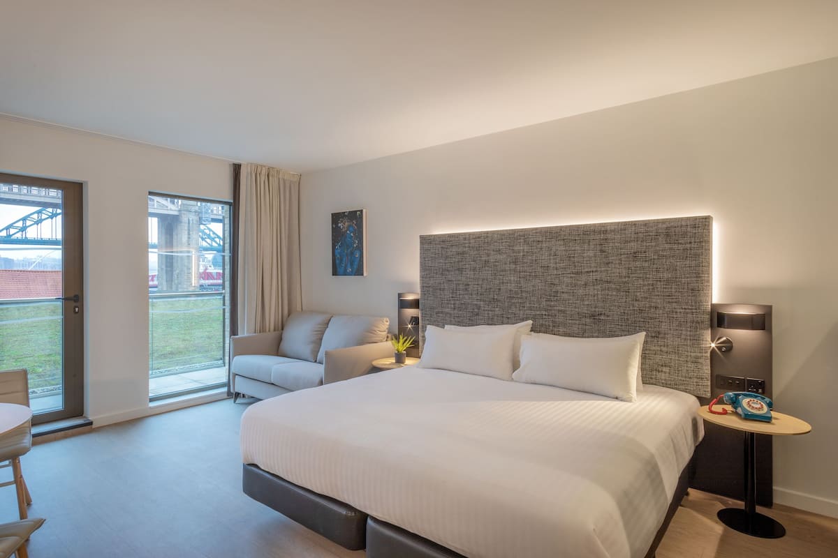 Une chambre d’hôtel moderne avec un grand lit, un canapé, un bureau et une vue sur un pont.