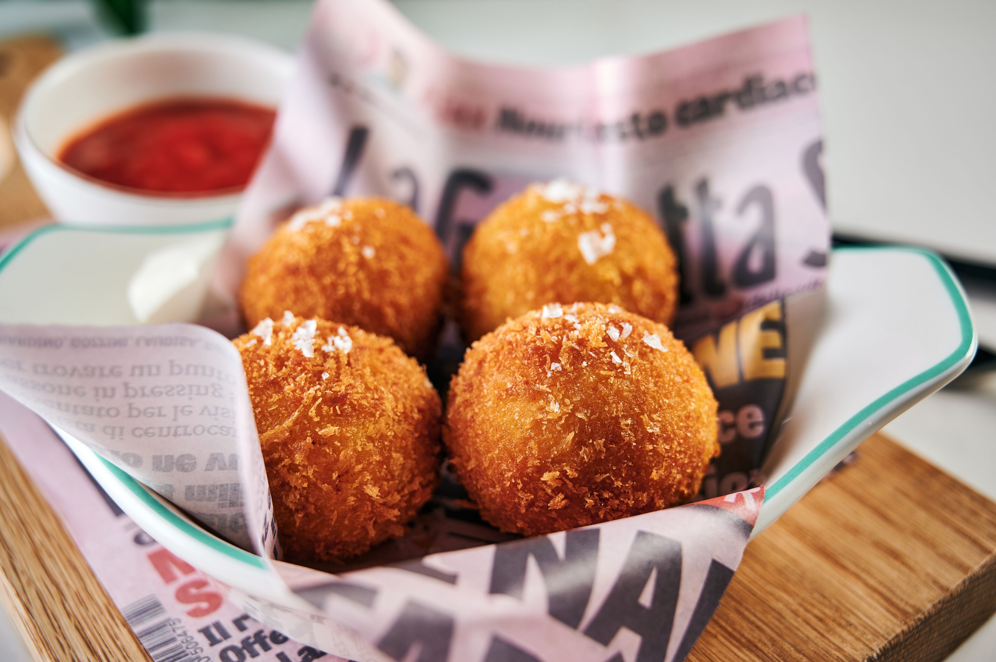 A tray of golden-brown fried balls, possibly croquettes, with a side of red dipping sauce.