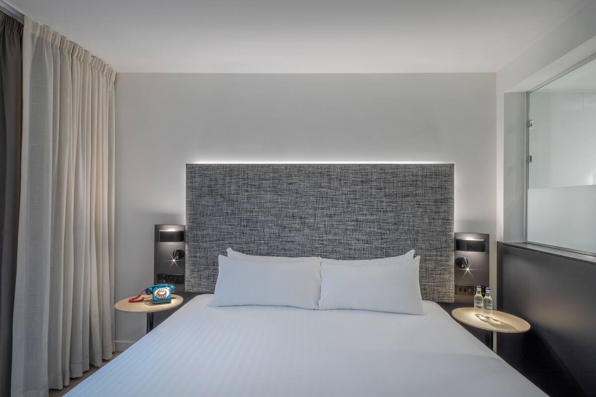 Une chambre d’hôtel avec un grand lit, deux tables de chevet, une tête de lit et un miroir au mur.