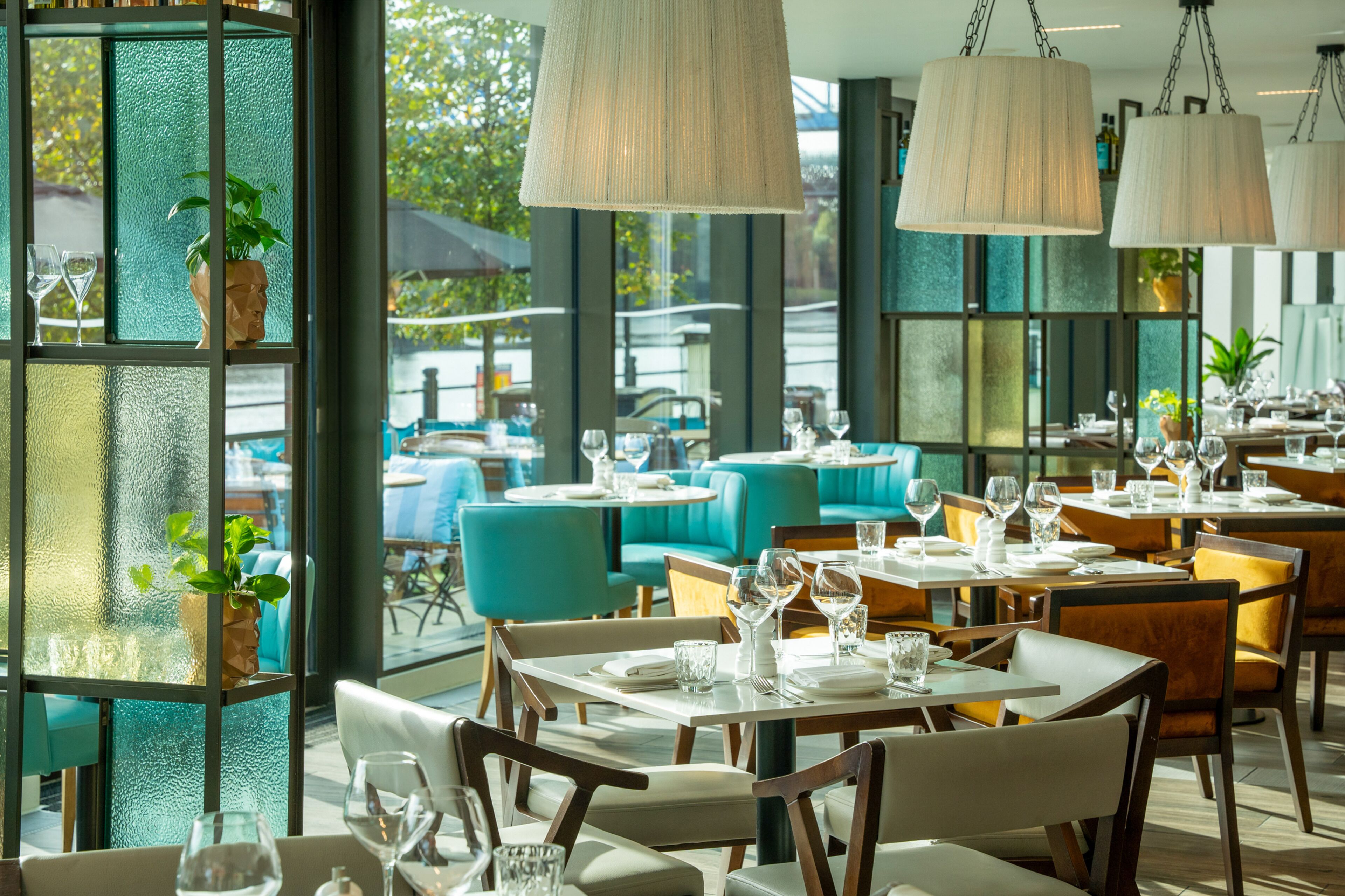 A restaurant with tables set for dining, large windows, and hanging light fixtures.