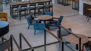 A modern interior with multiple seating areas, including round tables and sofas, and a high ceiling with hanging light fixtures.