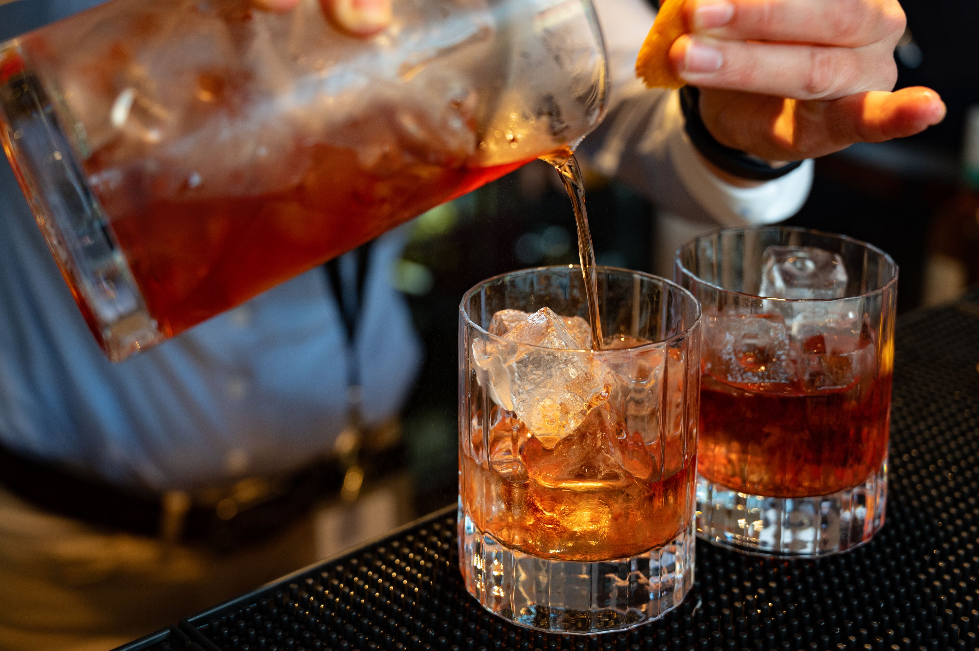 A person pouring a drink into two glasses on a table.