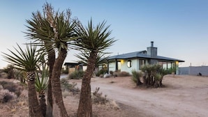 Una casa moderna con camino de tierra, palmeras y cielo despejado.