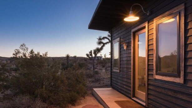 Una cabaña de madera con ventanas amplias, un camino de piedra y un paisaje desértico al fondo.