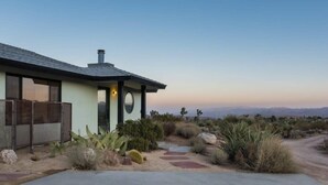 Una casa moderna con un amplio ventanal, una chimenea y un paisaje desértico.