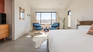Un dormitorio con una cama, dos sillones, una mesita, un televisor y una ventana con vistas.