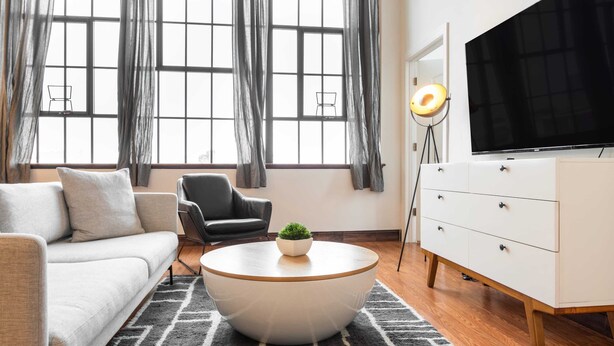 Una sala de estar moderna con un sofá, un sillón, una mesa de centro redonda, televisión y una lámpara.