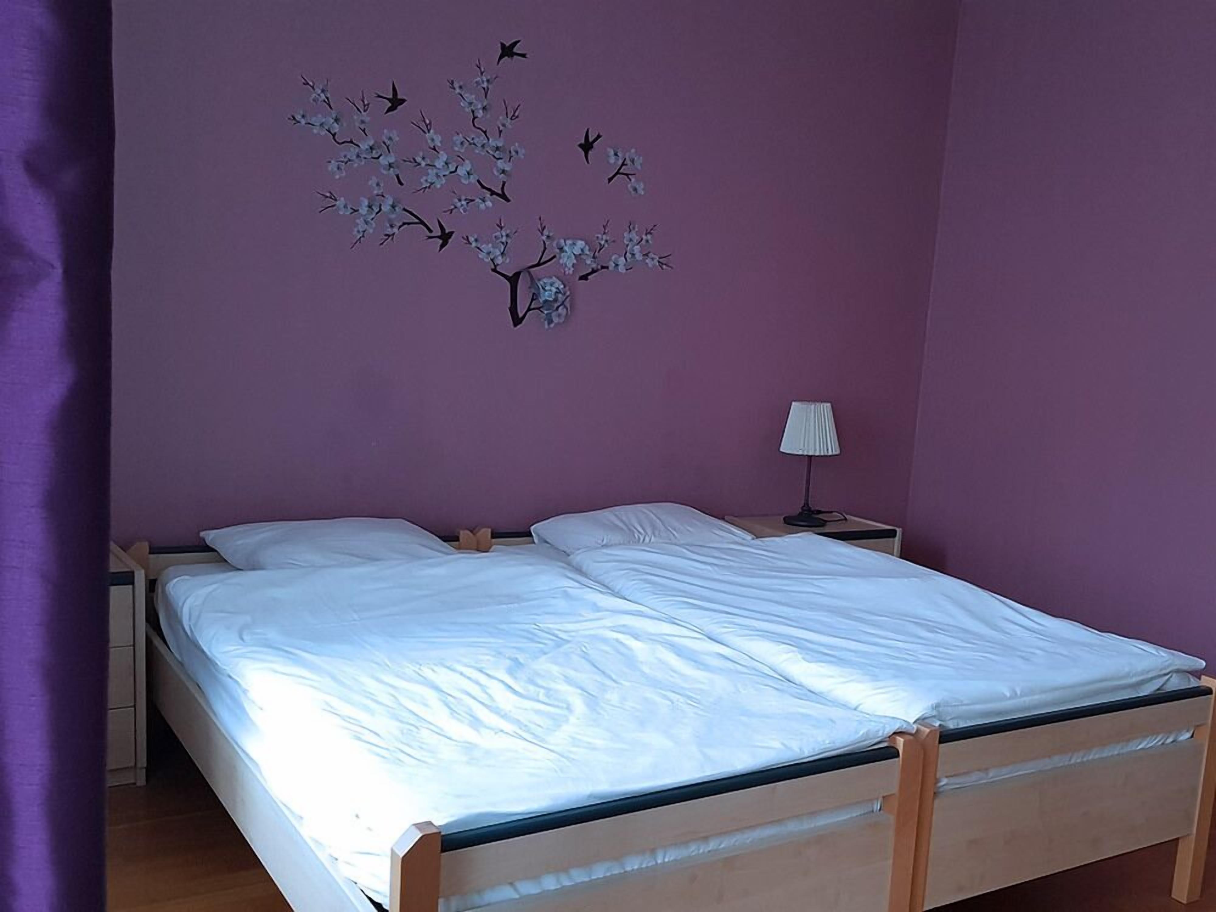 Un dormitorio con una cama doble, una mesita de noche con lámpara y una decoración de aves y flores en la pared.