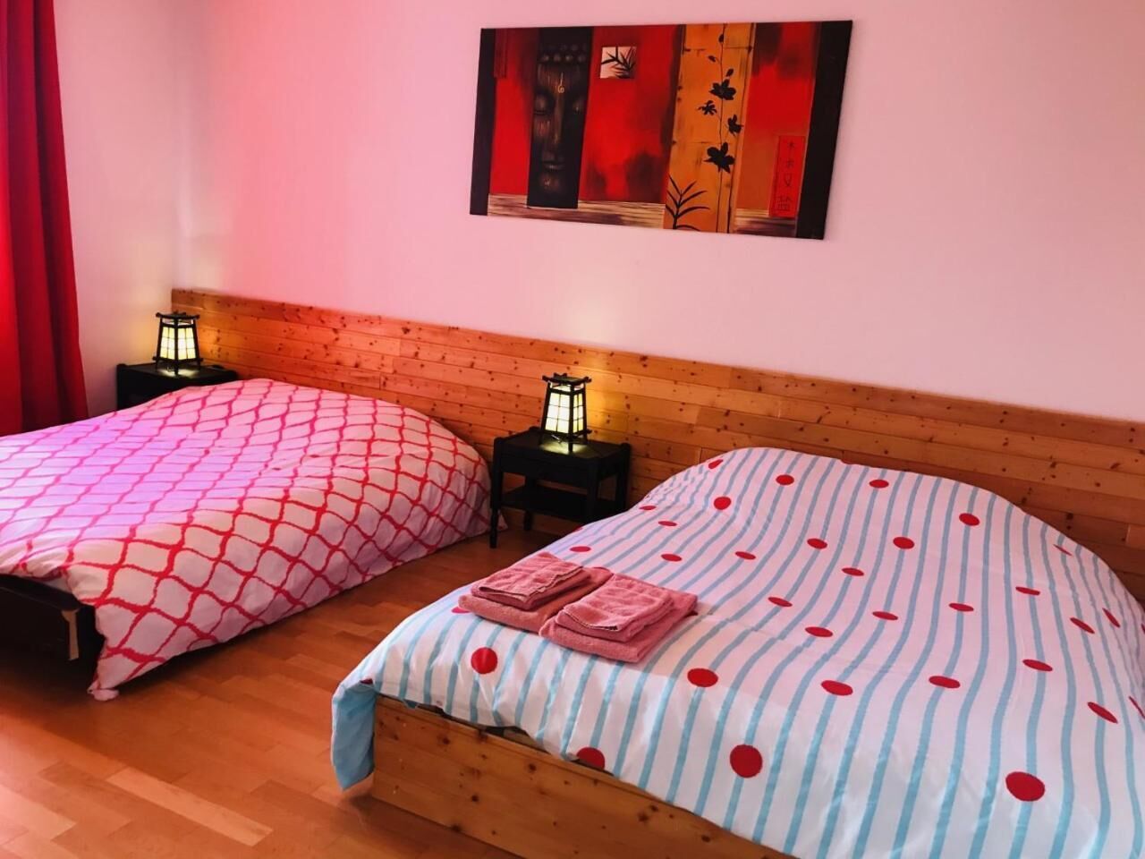 Two beds with patterned bedding, a wooden headboard, a nightstand with a lantern, and a painting on the wall.
