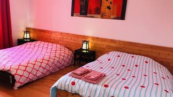 Two beds with patterned bedding, a wooden headboard, a nightstand with a lantern, and a painting on the wall.