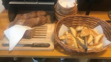 Un comptoir en bois avec une planche à découper, un panier de croissants et une pile de pains.
