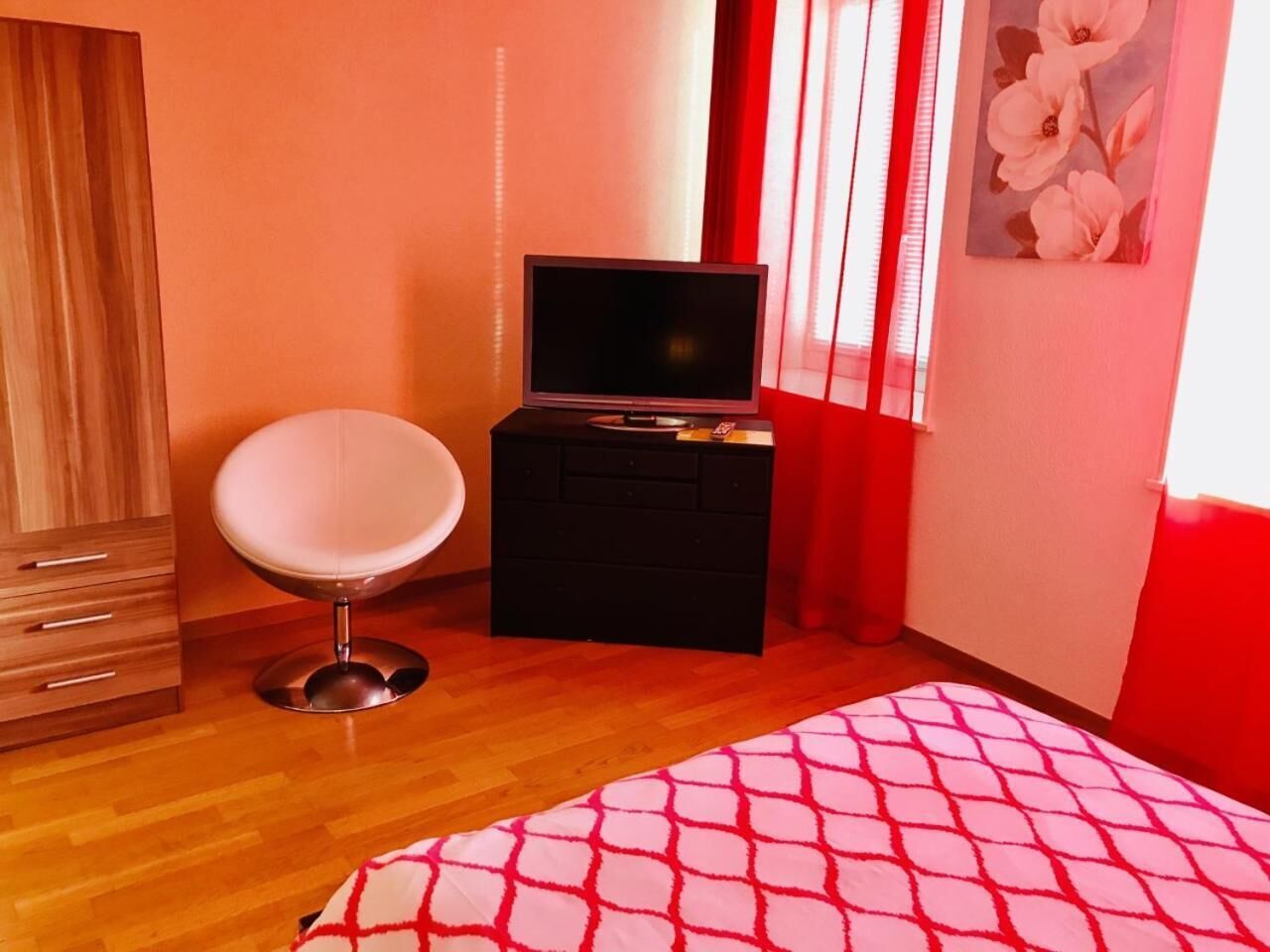A bedroom with a bed, a chair, a TV on a stand, and a wardrobe.