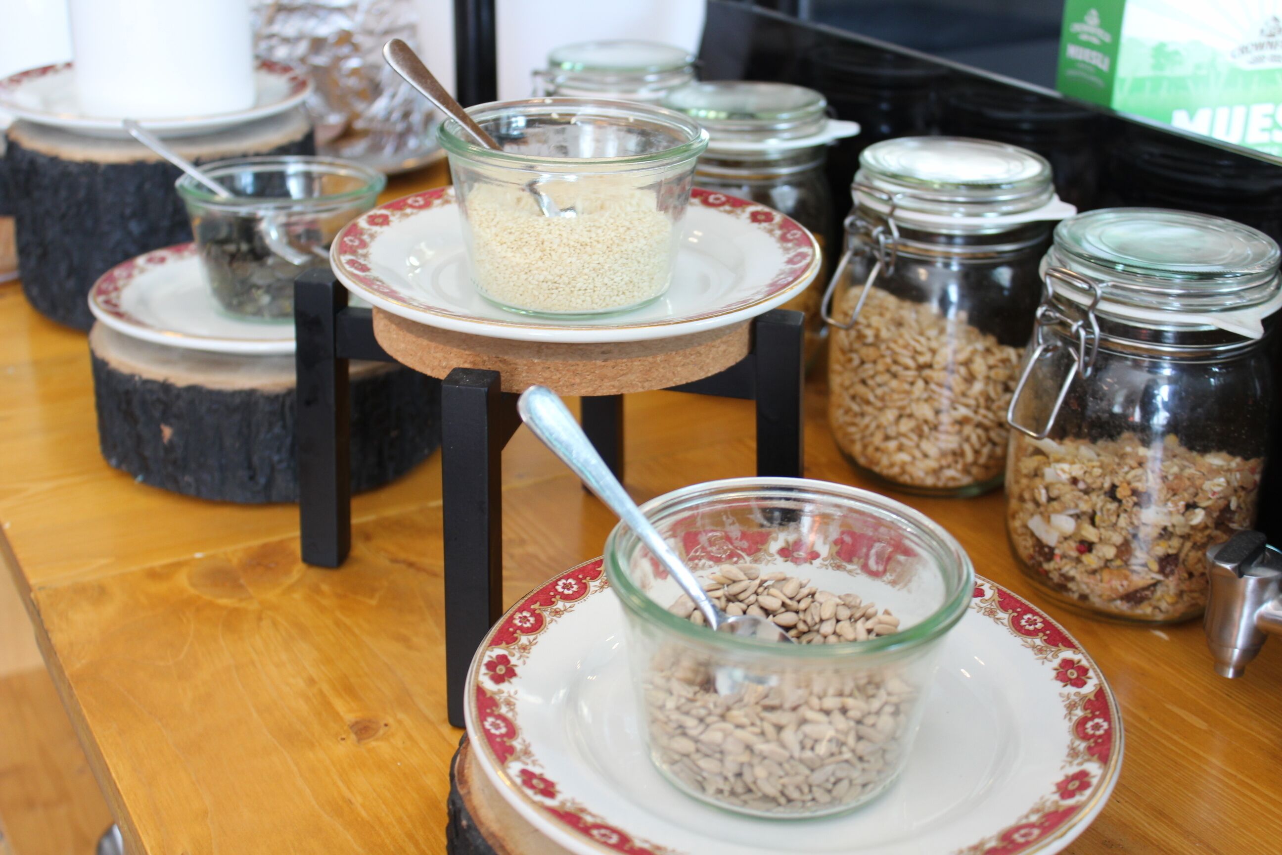 A table with glass jars containing various grains and seeds, each with a spoon.