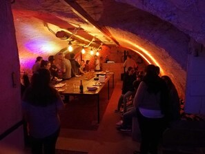 A dimly lit underground dining area with stone walls and a long table set for a meal. - Hotel de Ville (Les Verrieres)