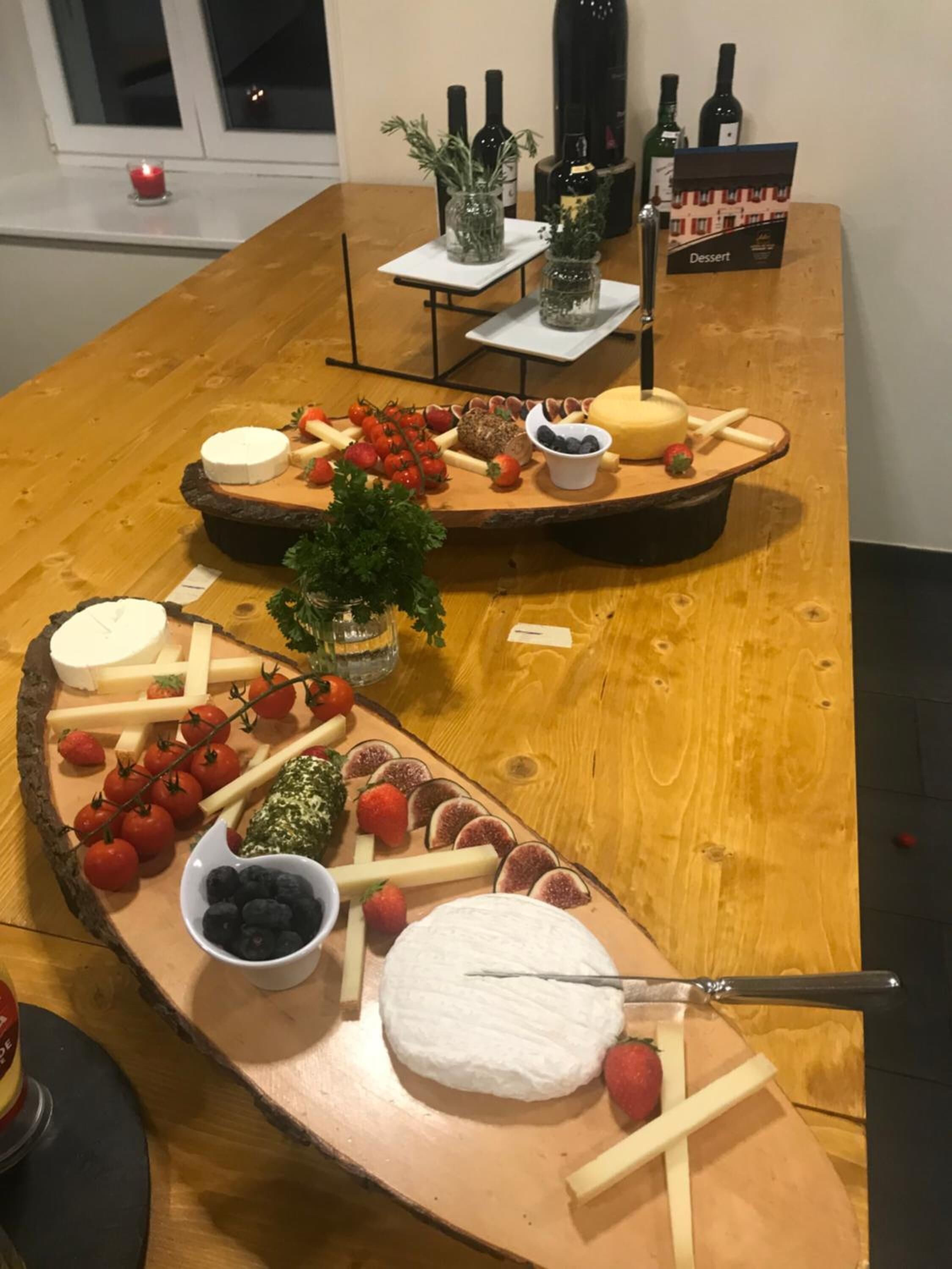 A wooden table with a variety of cheeses, fruits, and a small plant.