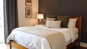 A neatly made bed with a white comforter and pillows, a bedside lamp, and framed pictures on the wall. - Home on the Range (Cookeville)