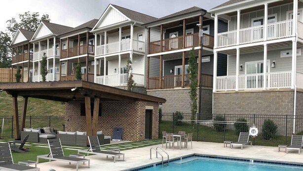 A multi-story building with balconies, a swimming pool with lounge chairs, and a covered patio area. - Home on the Range (Cookeville)