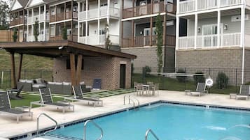 A multi-story building with balconies, a swimming pool with lounge chairs, and a covered patio area.