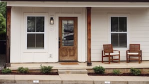 A two-story house with a front porch, two windows on the first floor, a wooden door, and two chairs on the porch. - Home on the Range (Cookeville)